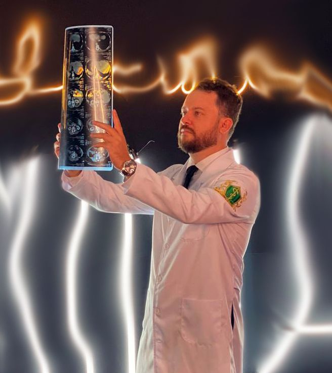 Dr. Raphael Alves Macedo de jaleco, analisando neuroimagem